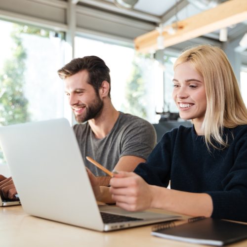 Image of concentrated young colleagues sitting in office coworking using laptop computers. Looking aside.